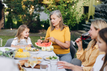 Grandmother serving watermelon to granddaughter at family gathering in garden