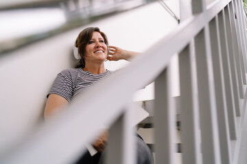 Relaxed woman enjoying meditation sound in headphones while sitting outdoors. Adult female listen to music in earphones