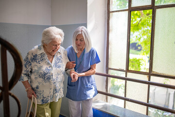 Female healthcare worker helping senior patient walking up the stairs.