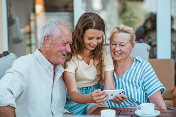 Granddaughter looking at photos in smartphone with older grandparents.