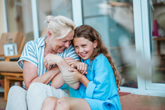Grandmother and granddaughter spending summer together, sitting in front of house.