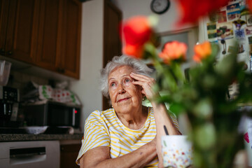 Portrait of worried senior woman sitting in kitchen.