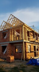 Fototapeta premium A new house under construction, with wooden framing and red brick, stands on a building site.