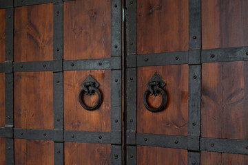 Antique wooden doors with intricate black metal reinforcement. Weathered wooden texture and ornate metalwork on handles showcase craftsmanship and resilience, history and artistry in unique design