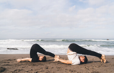 Two men link hands in deep plow pose—partnership, discipline, and breath control as metaphor for...