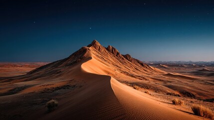 Naklejka premium A vast golden sand dune shaped like rolling waves dominates the desert landscape under a deep blue starry sky at twiligh