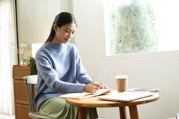 Young Asian woman enjoying a peaceful moment reading a book near window. Calm lifestyle, self-learning, and mindfulness at home.