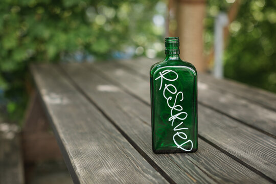 Close-up of a green glass bottle on a wooden table outdoors being used as a reserved sign