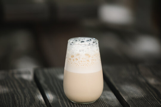 Close-up of an Iced coffee latte with frothy foam on a wooden garden table