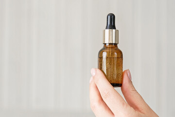 Naklejka premium Female hands showing natural oil cosmetics on a Beige Background. Dropper amber brown glass Bottle with pipette. Spa Beauty products Isolate on Neutral Backdrop. Skincare recommend, makeup advertising