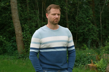 Handsome young man standing outdoors. Male thinking looking around feel happy, calm and serious. Green park background. Guy business employer, businessman manager inspired in nature. Diversity People