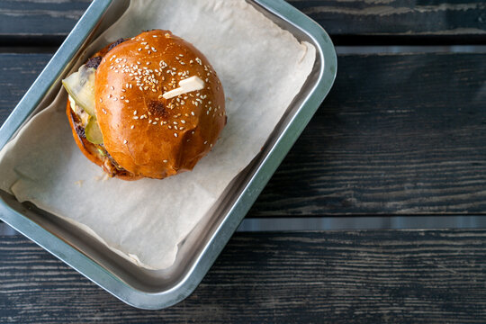 Close-up overhead view of a juicy cheeseburger with pickles and salad on a metal tray on an outdoors garden table