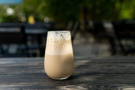 Close-up of an Iced coffee latte with frothy foam on a wooden garden table
