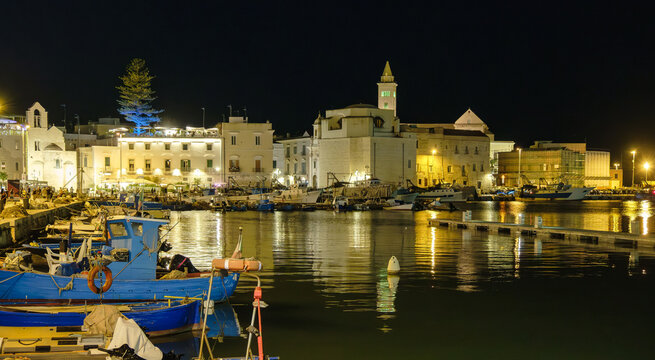 View into land across the harbour of illuminated townscape with the cathedral at night, Trani, Puglia, Italy