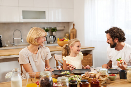 A family gathers around the dining table, sharing a delightful meal in a sunny kitchen. Conversations and laughter fill the air as they enjoy each other's company.