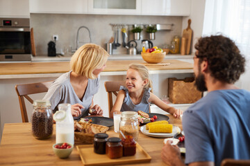 Three family members share a joyful breakfast experience in their bright kitchen, laughing and...
