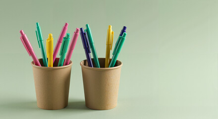 Colorful markers in brown cups on green background  