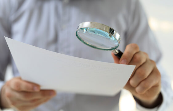Close-up of a businessman carefully reviewing a document using a magnifying glass. Focus, detail, precision. - Powered by Adobe