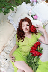 a beautiful girl with dark hair is lying on a bed in the yard. she is holding flowers in her hands