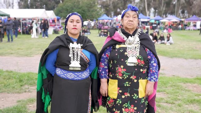 Two generations of mapuche women standing in traditional dresses for a portrait outdoors cultural event