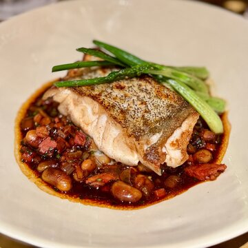 Close-up of a piece of roasted cod with a bean, bacon and red wine sauce