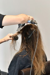 Fototapeta premium Parrucchiere asciuga i capelli di una cliente con phon professionale e spazzola 
