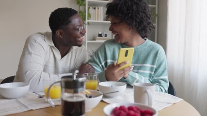 Cheerful couple watching smartphone content during breakfast in slow motion - Powered by Adobe