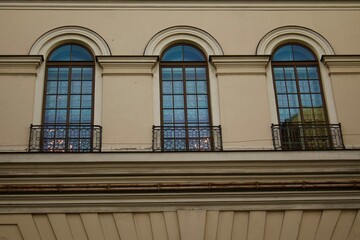 Three tall arched windows of a historic building with wrought iron balcony railings, reflecting the sky and city lights, emphasizing classical architecture elegance.