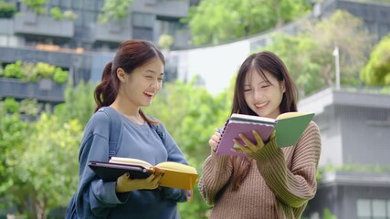Two young Asian female students enjoy a lively study session outside their university. They exchange ideas, smile, and laugh, showcasing the joy of learning together in a beautiful outdoor setting