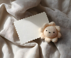 Cute baby announcement flat lay with blank scalloped card and soft plush flower toy on fabric background. Perfect for newborn greetings, invitations, or baby shower design.
