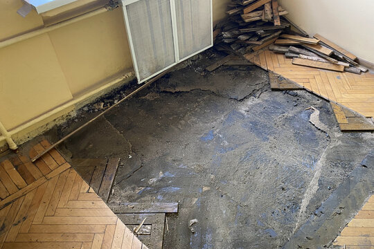 Close-up of partially removed wooden parquet flooring revealing worn concrete subfloor during indoor renovation and repair work in an old building.