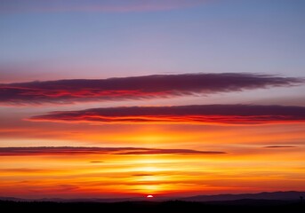 Obraz premium Vibrant sunset with horizontal cloud formations illuminating the twilight sky during golden hour displaying a radiant
