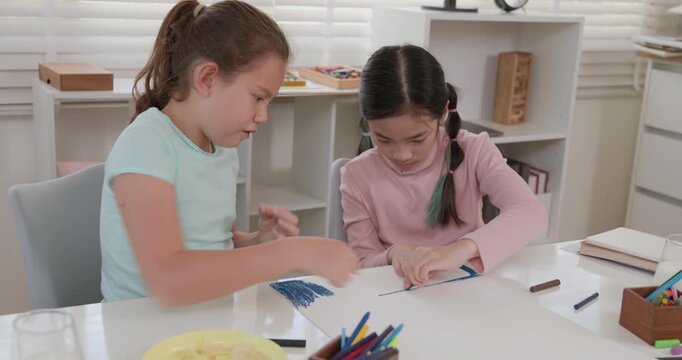 Children help each other color on paper on the table in classroom, 4k video.