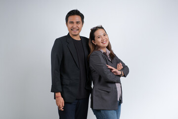 Smiling man and woman in formal attire standing back to back with crossed arms. Studio portrait on plain background representing teamwork.