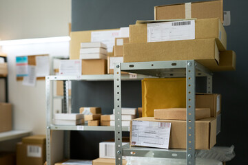 Cardboard boxes and padded envelopes stacked on metal shelving unit in warehouse setting, shipping...