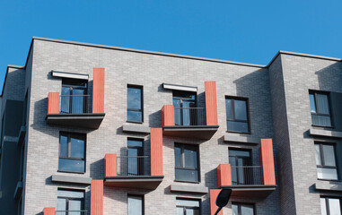 Modern residential building with gray brick facade, red vertical accents, and black balcony railings