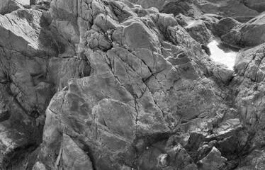 Monochrome photograph of rugged coastal rocks with sharp cracks and rough textures, highlighting