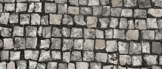 Stone pavement cobblestone surface with gray and beige square blocks, rough texture and weathered