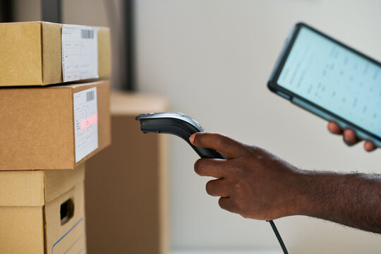 Black man scanning shipping labels on cardboard boxes with barcode scanner while holding digital tablet, focusing on logistics and inventory management in warehouse setting - Powered by Adobe
