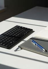 Minimalist desk setup featuring a black keyboard and a blue pen on a grey notebook