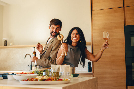 Happy couple enjoying drinks and fun while cooking dinner together