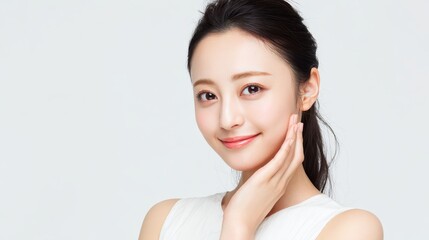 A lovely and beautiful Asian woman, fresh and youthful.
She gently touches her cheek with one hand in a natural pose.
She wears a simple white sleeveless top for a clean look against a white backgroun