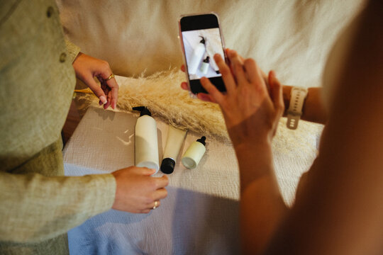 Two people photographing cosmetic bottles with a smartphone in a natural setting