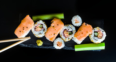 Top View of Selection of Salmon Sushi, Nigiri, Vegetable Hosomaki with Sesame Seeds, Celery, Wasabi on Slate Black Background, Japanese Cuisine
