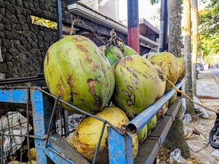 Fresh green coconuts piled high on a rustic cart, ready for sale on a tropical street.