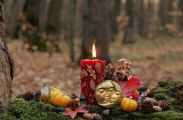 burning magic candle, moon amulet, crystals, decorative pumpkins in autumn forest. mystery fairy...