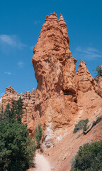 Fototapeta premium Imposing red rock formations tower over a desert path under a bright sky.