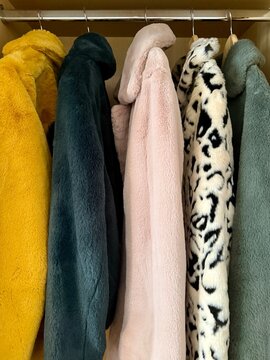 Close-up of five different coloured faux fur coats hanging in a wardrobe