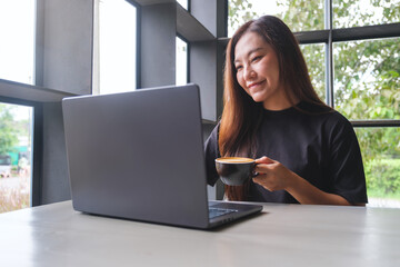 Portrait image of a woman working on laptop computer while drinking coffee