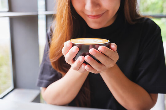 Closeup image of a beautiful young asian woman holding and drinking hot coffee in cafe